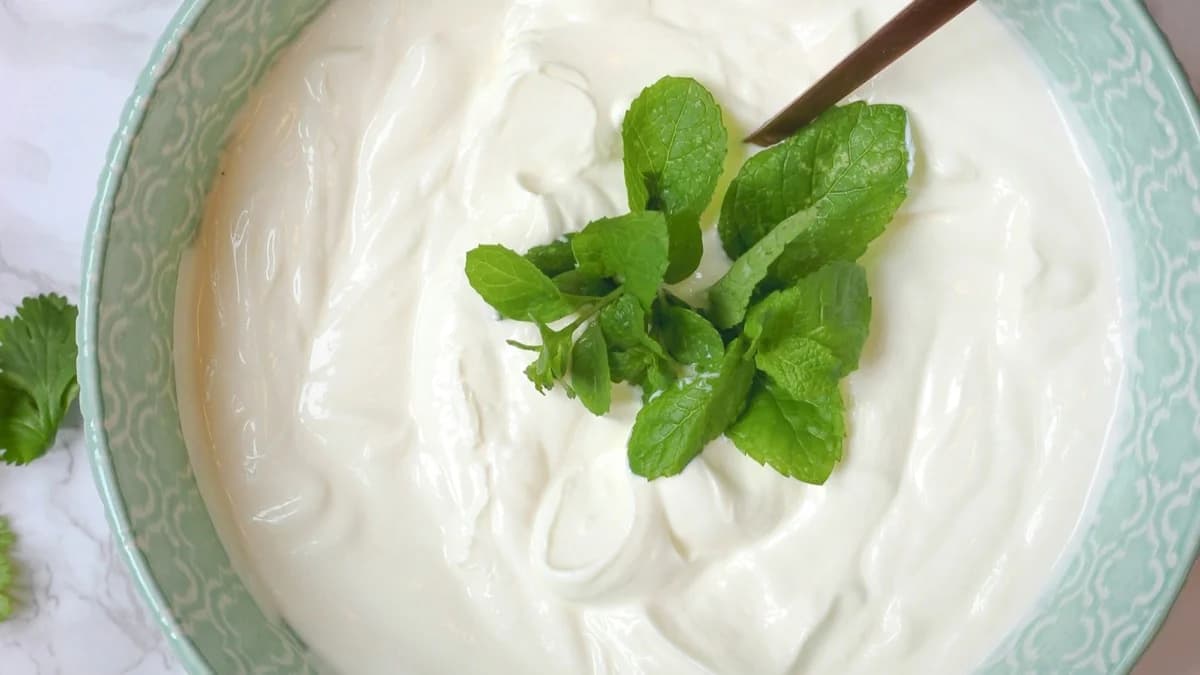 Bowl of plain yogurt with a spoon and mint garnish